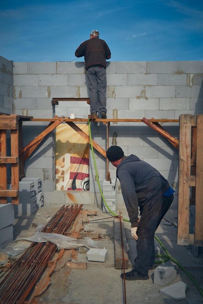 Two construction workers building a block wall on a sunny day at a construction site.